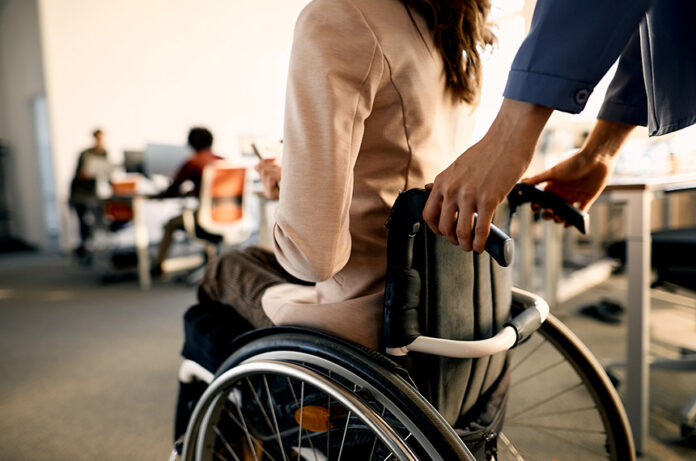 Close-up of colleague pushing businesswoman in wheelchair while arriving in the office.---------Pessoa, mulher, empurra mulher em cadeira de rodasFoto: iStockphoto