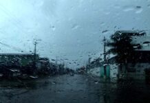 Chuvas atingem a Região Norte, mas o calor continua acima dos 35°C Visão através do para-brisa de um carro coberto por gotas de chuva, mostrando uma rua da cidade durante um dia de tempo fechado e nublado.