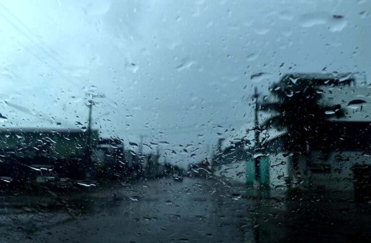 Chuvas atingem a Região Norte, mas o calor continua acima dos 35°C Visão através do para-brisa de um carro coberto por gotas de chuva, mostrando uma rua da cidade durante um dia de tempo fechado e nublado.