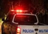 Área externa de um estabelecimento comercial com um homem caído no chão a receber assistência após uma ocorrência policial.