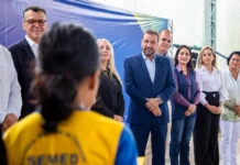 Hildon quer levar modelo de alfabetização de PVH ao estado O candidato Hildon Chaves, vestindo terno azul, sorri enquanto está rodeado por profissionais da educação e autoridades durante um evento em uma quadra escolar.