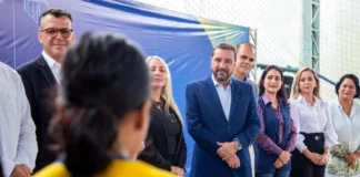 Hildon quer levar modelo de alfabetização de PVH ao estado O candidato Hildon Chaves, vestindo terno azul, sorri enquanto está rodeado por profissionais da educação e autoridades durante um evento em uma quadra escolar.