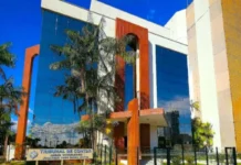 TCE-RO suspende licitação de R$ 1 milhão por restrições Fachada do prédio do Tribunal de Contas do Estado de Rondônia (TCE-RO), com arquitetura moderna, vidros espelhados azuis e detalhes em cor de madeira, cercado por palmeiras sob um céu azul.
