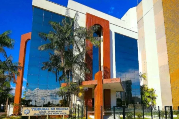 Fachada do prédio do Tribunal de Contas do Estado de Rondônia TCE-RO Fachada do prédio do Tribunal de Contas do Estado de Rondônia (TCE-RO), com arquitetura moderna, vidros espelhados azuis e detalhes em cor de madeira, cercado por palmeiras sob um céu azul.