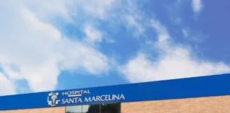 Fotografia da fachada do Hospital Santa Marcelina, destacando o prédio de tijolos aparentes com letreiro azul e branco e a entrada do setor Marcello Candia, sob um céu claro com nuvens.
