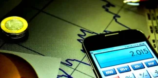 Mercado reduz previsão da Selic para 13,50% Máquina de calcular digital sobre gráficos financeiros, ilustrando os cálculos económicos do mercado.