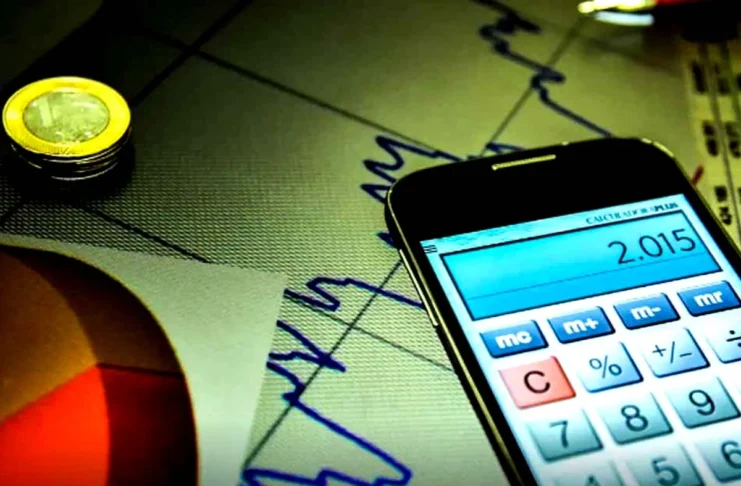Mercado reduz previsão da Selic para 13,50% Máquina de calcular digital sobre gráficos financeiros, ilustrando os cálculos económicos do mercado.