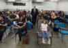 MPRO debate consumo consciente com acadêmicos de Direito O promotor de Justiça Alan Castiel Barbosa, de terno e gravata, posa sorridente em pé no fundo de uma sala de aula universitária, acompanhado por dezenas de estudantes de Direito acomodados em cadeiras azuis.