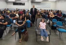 MPRO debate consumo consciente com acadêmicos de Direito O promotor de Justiça Alan Castiel Barbosa, de terno e gravata, posa sorridente em pé no fundo de uma sala de aula universitária, acompanhado por dezenas de estudantes de Direito acomodados em cadeiras azuis.