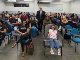 MPRO debate consumo consciente com acadêmicos de Direito O promotor de Justiça Alan Castiel Barbosa, de terno e gravata, posa sorridente em pé no fundo de uma sala de aula universitária, acompanhado por dezenas de estudantes de Direito acomodados em cadeiras azuis.