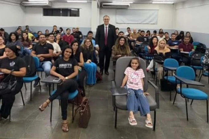 Promotor do MPRO com estudantes de Direito durante palestra em Porto Velho O promotor de Justiça Alan Castiel Barbosa, de terno e gravata, posa sorridente em pé no fundo de uma sala de aula universitária, acompanhado por dezenas de estudantes de Direito acomodados em cadeiras azuis.
