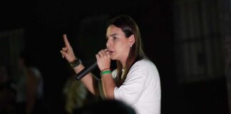Mariana Carvalho, candidata ao Senado, segura um microfone e discursa para o público durante um evento noturno de campanha.