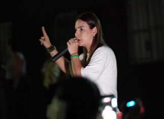 Mariana defende fronteira mais protegida para quem vive em Rondônia Mariana Carvalho, candidata ao Senado, segura um microfone e discursa para o público durante um evento noturno de campanha.