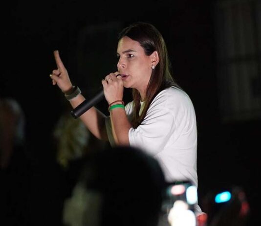Mariana defende fronteira mais protegida para quem vive em Rondônia Mariana Carvalho, candidata ao Senado, segura um microfone e discursa para o público durante um evento noturno de campanha.