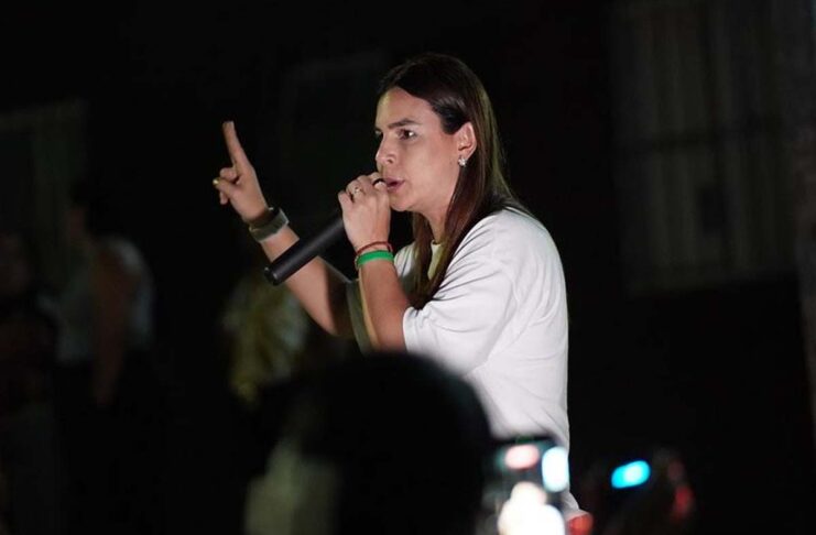 Mariana Carvalho, candidata ao Senado, segura um microfone e discursa para o público durante um evento noturno de campanha.
