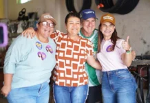 Mariana Carvalho, usando boné e camisa de campanha, sorri e abraça calorosamente três apoiadores durante um evento eleitoral no interior de Rondônia.