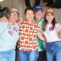 Mariana Carvalho, usando boné e camisa de campanha, sorri e abraça calorosamente três apoiadores durante um evento eleitoral no interior de Rondônia.
