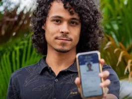 Prazo para baixar o e-Título termina no dia 3 de outubro Um jovem de cabelos cacheados sorri levemente enquanto exibe, em primeiro plano, a tela do seu celular com o aplicativo do e-Título aberto e validado.