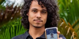 Prazo para baixar o e-Título termina no dia 3 de outubro Um jovem de cabelos cacheados sorri levemente enquanto exibe, em primeiro plano, a tela do seu celular com o aplicativo do e-Título aberto e validado.