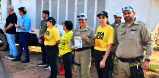 Rolim de Moura realiza ato cívico pelo Dia do Trânsito Agentes de trânsito e outros participantes, alguns vestindo camisetas amarelas, estão posicionados em uma rua durante um ato cívico em Rolim de Moura.