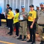 Agentes de trânsito e outros participantes, alguns vestindo camisetas amarelas, estão posicionados em uma rua durante um ato cívico em Rolim de Moura.