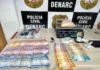 Denarc prende dupla e apreende 1kg de cocaína na Zona Sul Mesa com materiais apreendidos pela polícia, incluindo cédulas de dinheiro espalhadas, uma balança de precisão digital com um saco de substância branca e outros invólucros menores, em frente a um banner do DENARC - Polícia Civil.