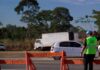 Funcionário com colete da Nova 364 a sinalizar a rodovia junto a barreiras de segurança e veículos em trânsito.