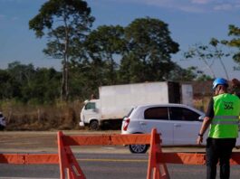 Funcionário com colete da Nova 364 a sinalizar a rodovia junto a barreiras de segurança e veículos em trânsito.