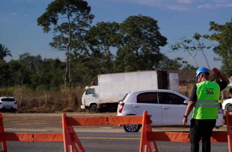 TJRO trava recurso da Nova 364 sobre buraco em rodovia Funcionário com colete da Nova 364 a sinalizar a rodovia junto a barreiras de segurança e veículos em trânsito.