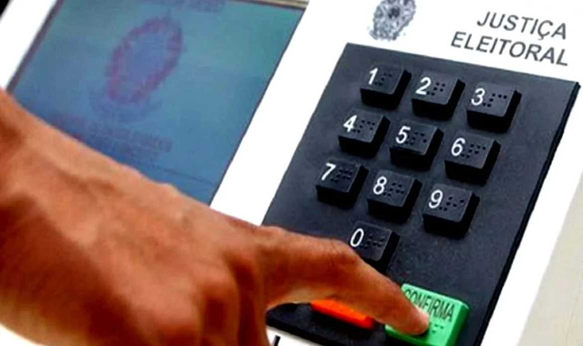 Dedo de um eleitor a pressionar a tecla verde de confirmação numa urna eletrónica da Justiça Eleitoral.