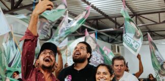 Os candidatos Jean Oliveira e Márcia Oliveira sorriem e celebram com apoiadores durante uma grande reunião política em Porto Velho.