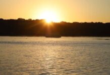 Meteorologia prevê domingo quente em Rondônia com termómetros a atingir os 36°C Fotografia de um pôr do sol alaranjado sobre um rio, ilustrando o clima quente da região.