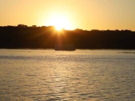 Meteorologia prevê domingo quente em Rondônia com termómetros a atingir os 36°C Fotografia de um pôr do sol alaranjado sobre um rio, ilustrando o clima quente da região.