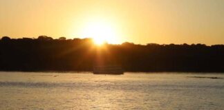 Fotografia de um pôr do sol alaranjado sobre um rio, ilustrando o clima quente da região.