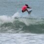Inscrições abertas para o 30º Circuito A Tribuna de Surf Colegial no Guarujá Uma surfista competidora, vestindo uma lycra rosa e parte de baixo preta, realiza uma manobra aérea sobre as ondas durante a bateria de surfe.