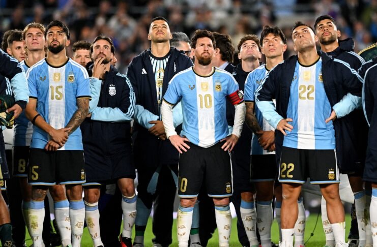 O jogador Lionel Messi em pé no gramado do estádio, olhando para o alto com uma expressão de claro desconforto e frustração.