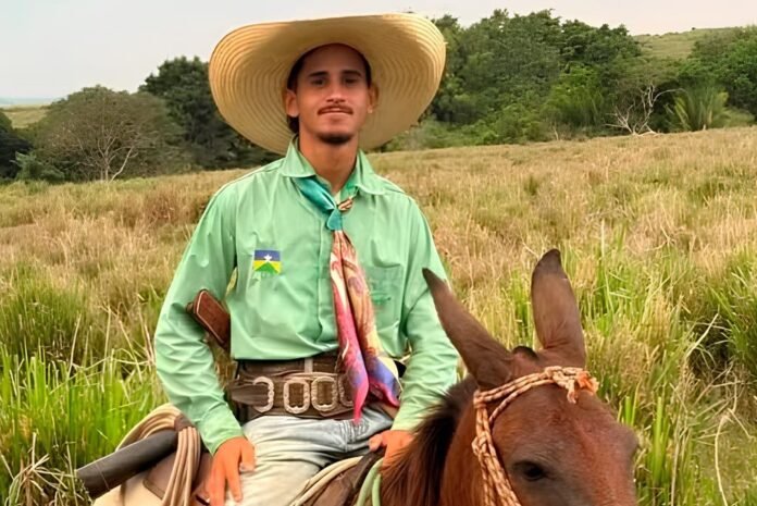 ovem Marcos André Ferreira Santos Fotografia do jovem Marcos André Ferreira Santos montado a cavalo, sorrindo e vestindo um chapéu de palha, camisa verde e lenço colorido no pescoço em uma área de pastagem.