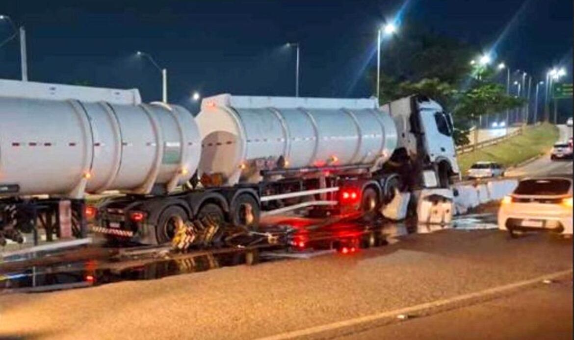 Camião-cisterna branco acidentado e imobilizado à noite após embater na mureta de proteção do viaduto, com grande quantidade de líquido espalhado e a refletir no asfalto.