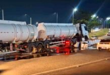 Camião-cisterna branco acidentado e imobilizado à noite após embater na mureta de proteção do viaduto, com grande quantidade de líquido espalhado e a refletir no asfalto.