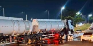 Camião-cisterna branco acidentado e imobilizado à noite após embater na mureta de proteção do viaduto, com grande quantidade de líquido espalhado e a refletir no asfalto.