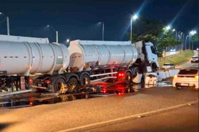 Camião-cisterna branco acidentado e imobilizado à noite após embater na mureta de proteção do viaduto, com grande quantidade de líquido espalhado e a refletir no asfalto.
