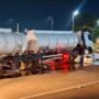 Camião-cisterna branco acidentado e imobilizado à noite após embater na mureta de proteção do viaduto, com grande quantidade de líquido espalhado e a refletir no asfalto.