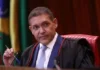 TSE determina suspensão de canal de André Janones no WhatsApp a pedido de Flávio Bolsonaro O ministro Kassio Nunes Marques, presidente do TSE, vestindo toga preta e gravata azul, segurando uma caneta durante uma sessão no tribunal.