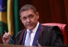 TSE determina suspensão de canal de André Janones no WhatsApp a pedido de Flávio Bolsonaro O ministro Kassio Nunes Marques, presidente do TSE, vestindo toga preta e gravata azul, segurando uma caneta durante uma sessão no tribunal.