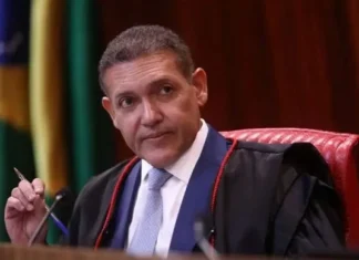 TSE determina suspensão de canal de André Janones no WhatsApp a pedido de Flávio Bolsonaro O ministro Kassio Nunes Marques, presidente do TSE, vestindo toga preta e gravata azul, segurando uma caneta durante uma sessão no tribunal.
