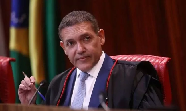 Ministro do TSE Kassio Nunes Marques O ministro Kassio Nunes Marques, presidente do TSE, vestindo toga preta e gravata azul, segurando uma caneta durante uma sessão no tribunal.
