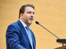 Deputado Alex Redano agradece apoio nas urnas e renova compromissos sociais O deputado estadual Alex Redano a discursar num púlpito ao microfone, envergando um fato azul-escuro e gravata azul-clara.