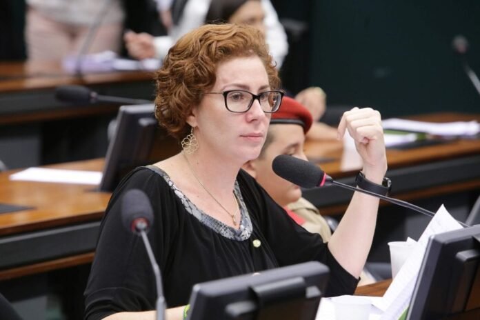 A ex-deputada federal Carla Zambelli, vestindo trajes formais, falando ao microfone durante uma sessão parlamentar.