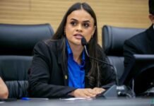 A deputada estadual Dra. Taíssa Sousa a discursar ao microfone durante uma sessão parlamentar, envergando um casaco escuro e uma camisa azul.