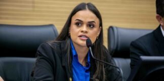 A deputada estadual Dra. Taíssa Sousa a discursar ao microfone durante uma sessão parlamentar, envergando um casaco escuro e uma camisa azul.